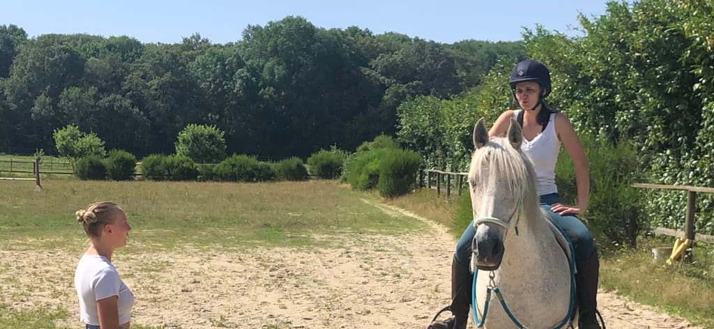 Cours d'équitation en carrière dans les Yvelines : cavalière sur un cheval gris guidée à la voix